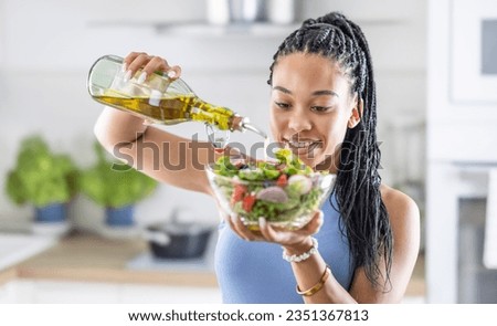 A young African American woman prepares a healthy leafy salad, tossing it with olive oil.