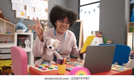 Young african american woman preschool teacher reading story book on video call at kindergarten - Shutterstock ID 2338747987