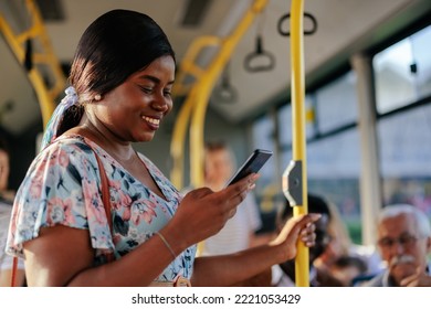 A young african american woman is in a public bus holding onto a pole and looking at her smarptphone - Powered by Shutterstock