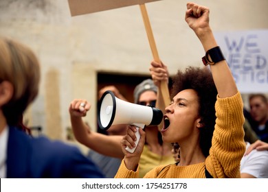 Young African American Woman With Raised Fist Shouting Through Megaphone While Being On Anti-racism Protest. 