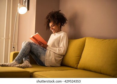 Young african american woman reading a book at home.