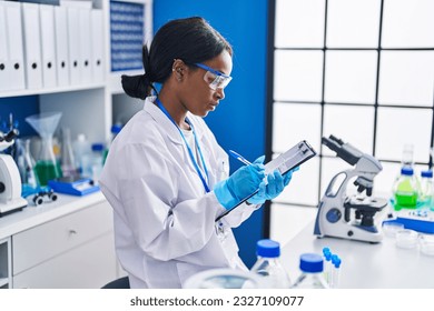 Young african american woman scientist writing on document at laboratory