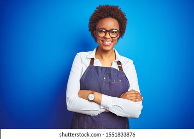 Young African American Woman Shop Owner Wearing Business Apron Over Blue Background Happy Face Smiling With Crossed Arms Looking At The Camera. Positive Person.