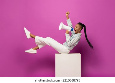Young African American woman shouting on megaphone and raising fist in studio purple pink color isolated background - Shutterstock ID 2210568795