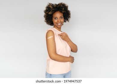 Young African American Woman Showing Her Arm With Band Aid After Coronavirus COVID-19 Vaccine Injection, Isolated On Gray Background