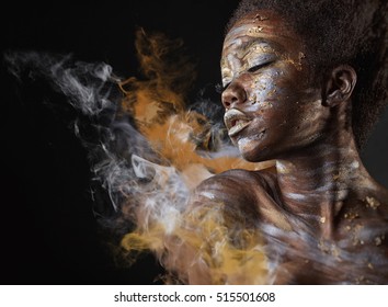 Young African American Woman With Silver And Gold Make-up And Body Art On A Black Background With Smoke