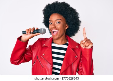 Young African American Woman Singing Song Using Microphone Surprised With An Idea Or Question Pointing Finger With Happy Face, Number One 