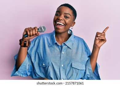 Young African American Woman Singing Song Using Microphone Smiling Happy Pointing With Hand And Finger To The Side 