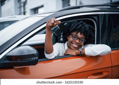 Young African American Woman Sits Inside Of New Modern Car With Keys In Hand.