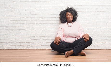 Young african american woman sitting on the floor wearing headphones looking away to side with smile on face, natural expression. Laughing confident. - Powered by Shutterstock