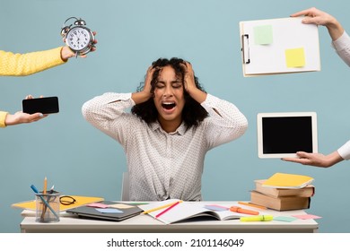 Young African American woman sitting at desk surrounded by hands with alarm clock and gadgets, screaming in despair, feeling exhausted, suffering from burnout. Multitasking, work life balance concept