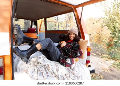 Young African American Woman Sitting At Table Near Car In Autumn Forest And Drinking Hot Tea, Dreamy Mixed Race Female Relaxing Around Campsite, Spending Time In Nature. Camping, Travel And Vanlife