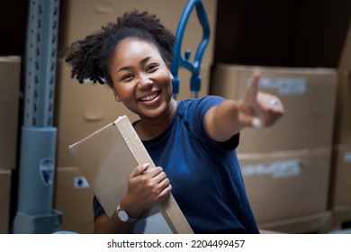 Young African American Woman Sitting On Trolley And Hold Box In Hand Which Pick Up From Shelf In DIY Warehouse And Pointing The New Shipment. Customer Service Yourself To Find Boxes By Using Code