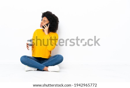 Young African American woman sitting on the floor holding coffee to take away and a mobile