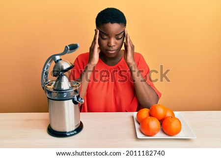 Young african american woman sitting on the table using juicer suffering from headache desperate and stressed because pain and migraine. hands on head. 