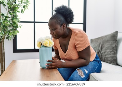 Young African American Woman Smelling Flowers Sitting On Sofa At Home