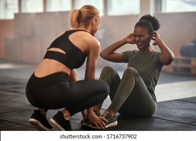 Young African American Woman Smiling While Doing Sit-ups With A Workout Partner On The Floor Of A Gym