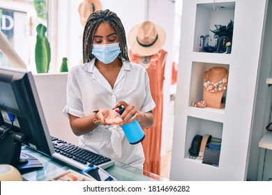 Young African American Woman Smiling Happy Working At The Till Wearing Coronavirus Safety Mask And Using Sanitizer Gel At Retail Shop