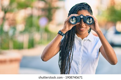 Young african american woman smiling happy looking for new opportunity using binoculars at the city. - Powered by Shutterstock