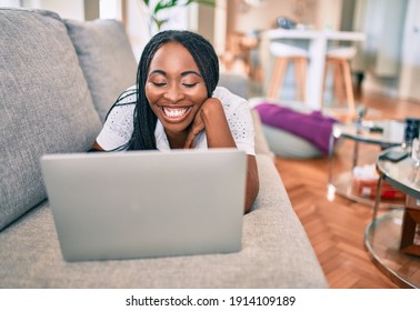 Young African American Woman Smiling Happy Working Using Laptop Laying On The Sofa At Home