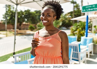 Young African American Woman Smiling Happy On A Summer Day By Bar Terrace Eating An Ice Cream