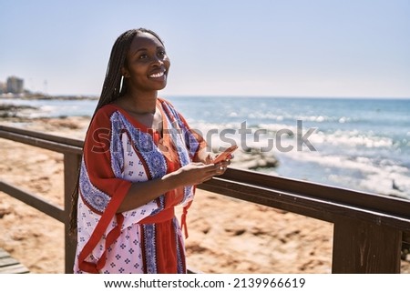 Young african american woman smiling happy using smartphone at the beach.