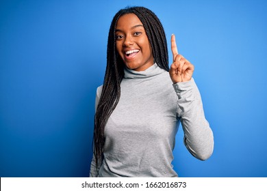 Young african american woman standing wearing casual turtleneck over blue isolated background pointing finger up with successful idea. Exited and happy. Number one.