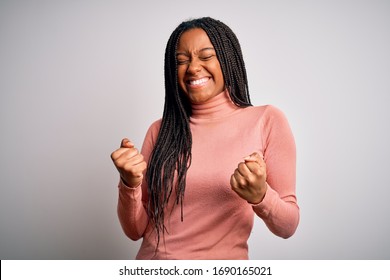 Young african american woman standing casual and cool over white isolated background very happy and excited doing winner gesture with arms raised, smiling and screaming for success. Celebration