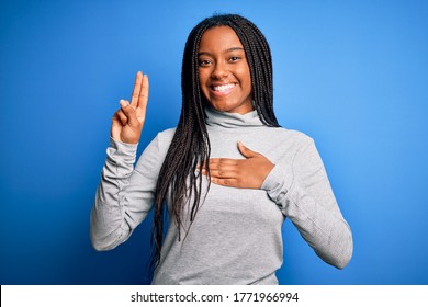 Young african american woman standing wearing casual turtleneck over blue isolated background smiling swearing with hand on chest and fingers up, making a loyalty promise oath - Shutterstock ID 1771966994