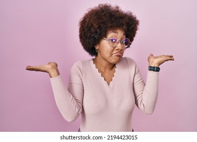 Young African American Woman Standing Over Pink Background Clueless And Confused Expression With Arms And Hands Raised. Doubt Concept. 