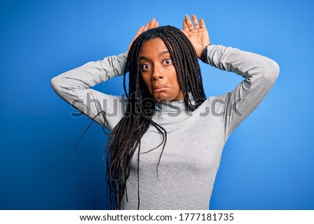 Young african american woman standing wearing casual turtleneck over blue isolated background Doing bunny ears gesture with hands palms looking cynical and skeptical. Easter rabbit concept.