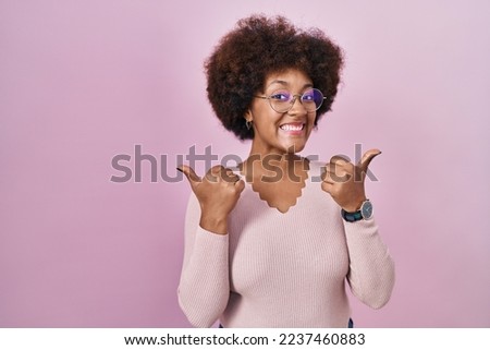 Young african american woman standing over pink background success sign doing positive gesture with hand, thumbs up smiling and happy. cheerful expression and winner gesture. 