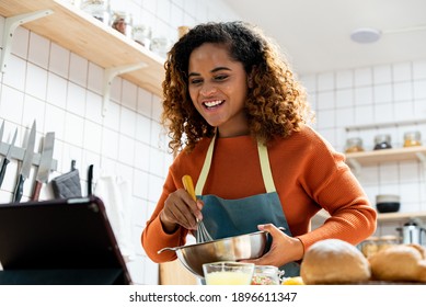 Young African American woman streaming live video teaching bakery cooking online in kitchen at home - Powered by Shutterstock