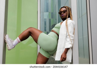 Young african american woman with sunglasses looking at camera leaning against wall with leg up on wall. Copy space.
