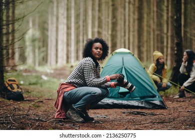 Young African American woman taking photos with a telephoto lens while camping with friends in a forest - Powered by Shutterstock