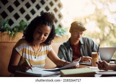 Young African American Woman Taking Notes While Studying With Friends In A Cafe,