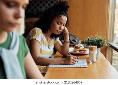 Young African American Woman Taking Notes While Studying In A Cafe.