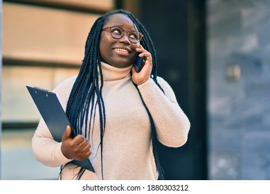 Young african american woman talking on the smartphone and holding clipboard at the city.