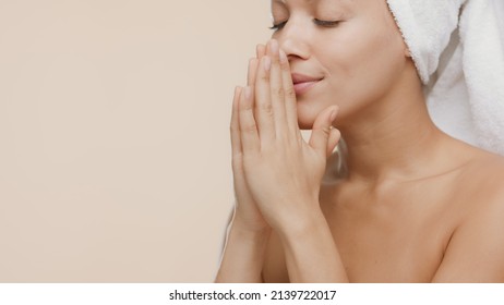 Young African American woman with a towel on her head put her hands together palm to palm and smells them enjoying the fragrance on beige background | Hand care commercial concept - Powered by Shutterstock