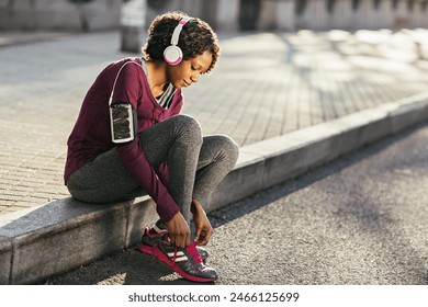 Young African American woman tying shoe laces before running in city park - Powered by Shutterstock