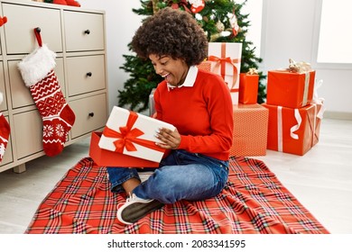 Young African American Woman Unboxing Gift Sitting By Christmas Tree At Home