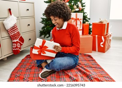 Young african american woman unboxing gift sitting by christmas tree at home - Powered by Shutterstock