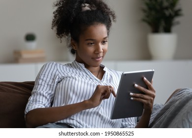 Young African American Woman Use Tablet Text Or Message Online On Gadget At Home. Happy Millennial Biracial Female Relax On Sofa Browse Wireless Internet Or Shopping On Pad Device. Technology Concept.