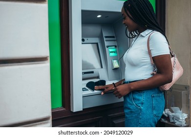 Young african american woman using credit card and atm machine while withdrawing money