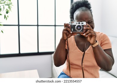 Young African American Woman Using Vintage Camera Sitting On Sofa At Home