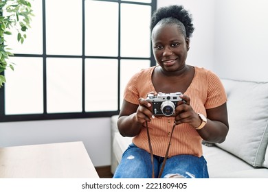 Young African American Woman Using Vintage Camera Sitting On Sofa At Home