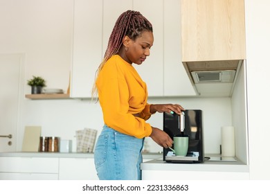 Young african american woman using modern coffee machine, making drink in the morning, standing in kitchen at home, free copy space, side view shot - Powered by Shutterstock