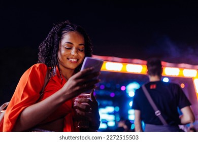 Young african american woman using a smartphone while standing in a crowd at music festival - Powered by Shutterstock