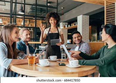 Young African American Woman Waitress Taking Orders From Clients In Cafe