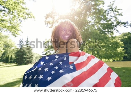 Young African american woman is waving American flag on top of at nature background. USA resident, US citizen. Immigration concept	                              